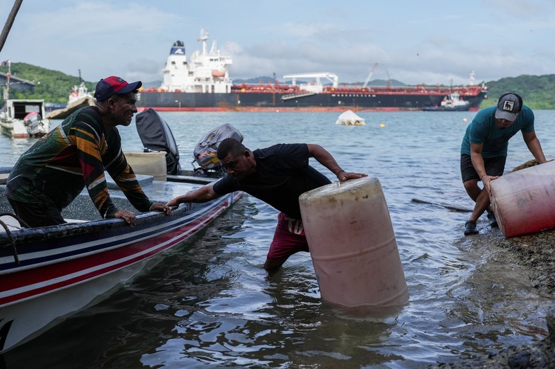 Para nelayan dari pelabuhan La Boca memuat tangki bensin ke atas perahu saat kapal berbendera Liberia, MSC ILLINOIS VII, melintasi Terusan Panama di tengah penurunan permukaan air akibat kurangnya curah hujan yang terkait dengan El Ni&ntilde;o, di Panama City, Panama, pada 4 September 2026. (REUTERS/Enea Lebrun)