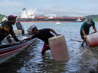 Para nelayan dari pelabuhan La Boca memuat tangki bensin ke atas perahu saat kapal berbendera Liberia, MSC ILLINOIS VII, melintasi Terusan Panama di tengah penurunan permukaan air akibat kurangnya curah hujan yang terkait dengan El Nio, di Panama Cit