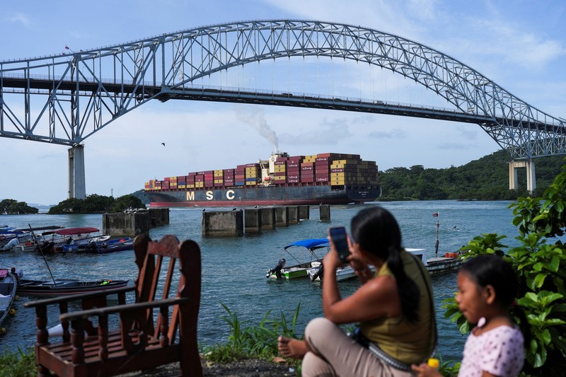 Para nelayan dari pelabuhan La Boca memuat tangki bensin ke atas perahu saat kapal berbendera Liberia, MSC ILLINOIS VII, melintasi Terusan Panama di tengah penurunan permukaan air akibat kurangnya curah hujan yang terkait dengan El Ni&ntilde;o, di Panama City, Panama, pada 4 September 2026. (REUTERS/Enea Lebrun)