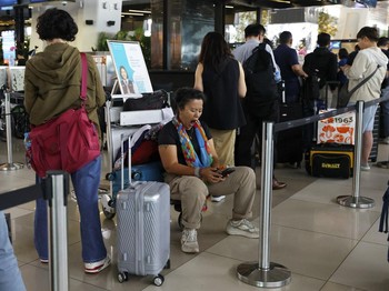 Seorang penumpang yang terlantar duduk di atas troli bagasi di area layanan pelanggan Bandara Internasional Soekarno-Hatta setelah bandara tersebut menghentikan operasionalnya akibat letusan Gunung Anak Krakatau, di Tangerang, dekat Jakarta, Indonesi
