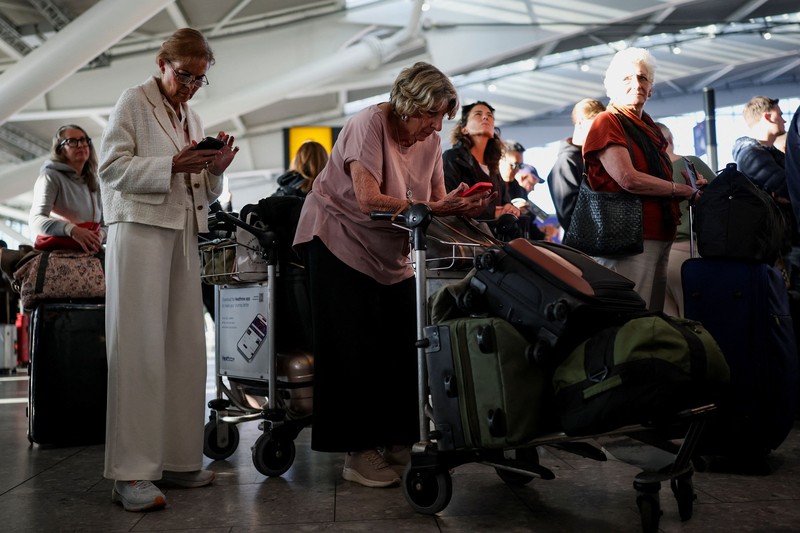 Stranded passengers use their phones after some departing flights were cancelled, at Heathrow Airport's Terminal 5 in London, Britain, September 8, 2026. Some departing flights at major British airports were disrupted on Tuesday after air traffic control provider NATS experienced a technical issue, with Heathrow, Gatwick, Manchester and Stansted among the airports affected by restrictions and delays. REUTERS/Isabel Infantes