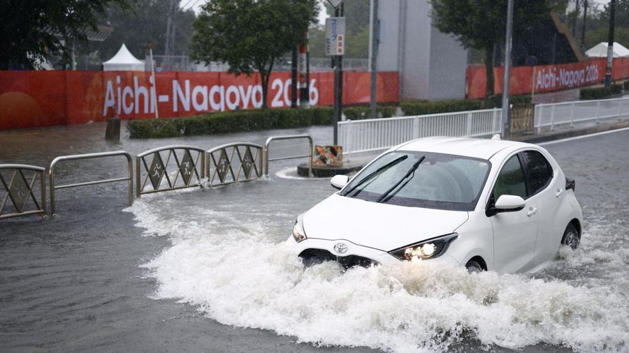 Sebuah mobil melaju di jalan yang tergenang akibat hujan deras, sementara spanduk Asian Games Aichi-Nagoya terlihat di latar belakang di Nagoya, Jepang tengah, pada 8 September 2026, dalam foto yang diambil oleh Kyodo ini. (Mandatory credit Kyodo/via