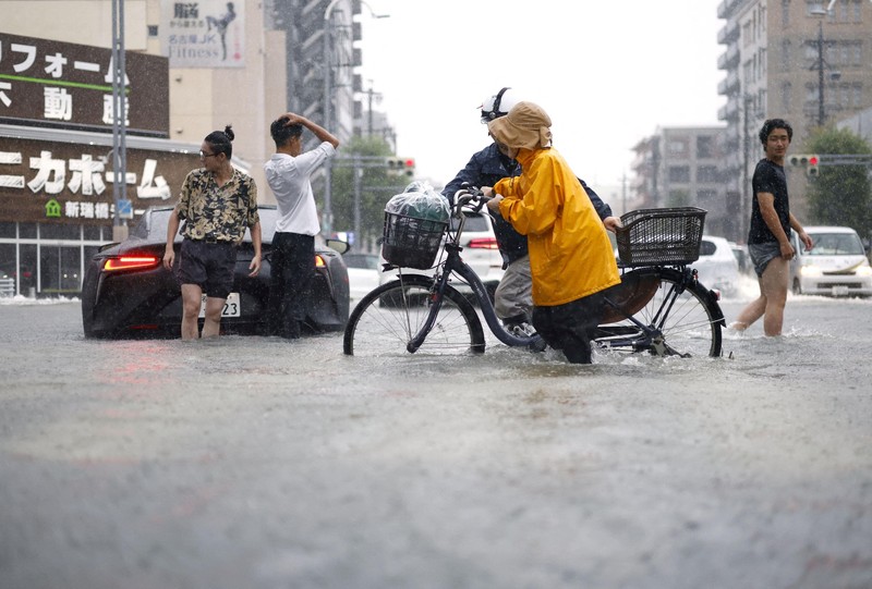 Sebuah mobil melaju di jalan yang tergenang akibat hujan deras, sementara spanduk Asian Games Aichi-Nagoya terlihat di latar belakang di Nagoya, Jepang tengah, pada 8 September 2026, dalam foto yang diambil oleh Kyodo ini. (Mandatory credit Kyodo/via REUTERS)