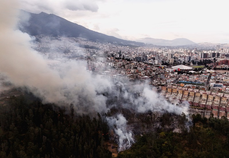 Kebakaran hutan di dekat kawasan permukiman, sementara orang-orang bermain sepak bola di sebuah lapangan di Quito, Ekuador, Minggu (13/9/2026). (REUTERS/Karen Toro)