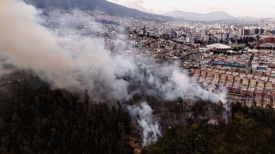 Kebakaran hutan di dekat kawasan permukiman, sementara orang-orang bermain sepak bola di sebuah lapangan di Quito, Ekuador, Minggu (13/9/2026). (REUTERS/Karen Toro)