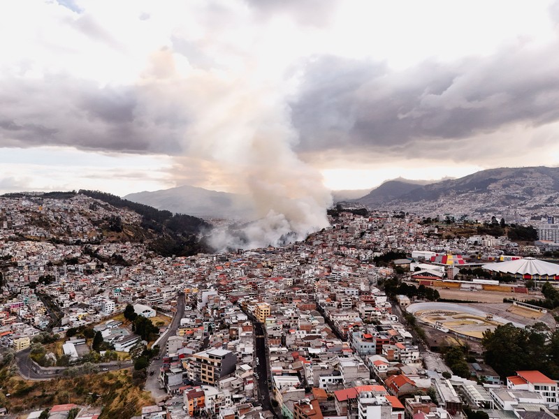 Kebakaran hutan di dekat kawasan permukiman, sementara orang-orang bermain sepak bola di sebuah lapangan di Quito, Ekuador, Minggu (13/9/2026). (REUTERS/Karen Toro)