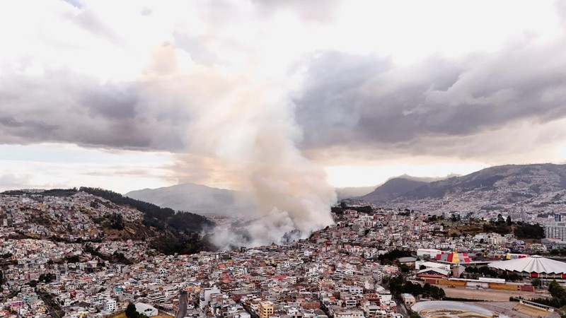Kebakaran hutan di dekat kawasan permukiman, sementara orang-orang bermain sepak bola di sebuah lapangan di Quito, Ekuador, Minggu (13/9/2026). (REUTERS/Karen Toro)