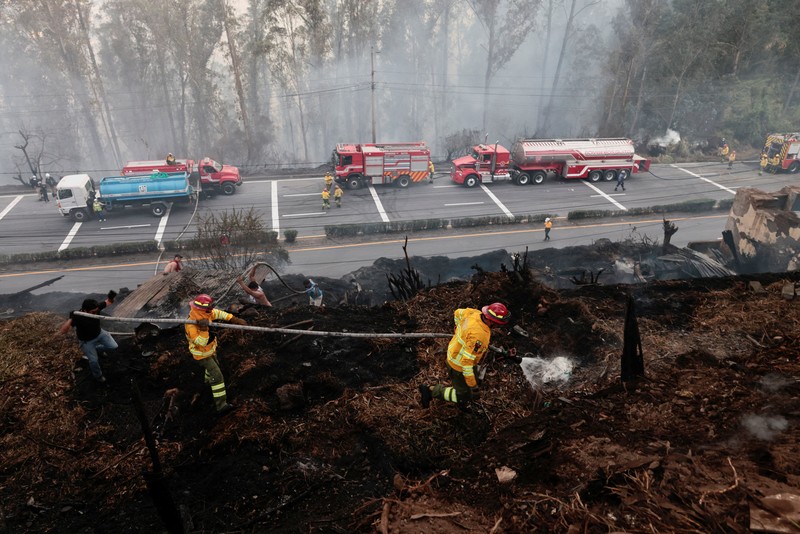 Kebakaran hutan di dekat kawasan permukiman, sementara orang-orang bermain sepak bola di sebuah lapangan di Quito, Ekuador, Minggu (13/9/2026). (REUTERS/Karen Toro)