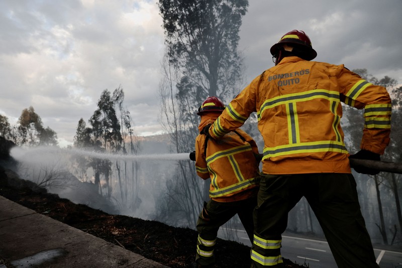Kebakaran hutan di dekat kawasan permukiman, sementara orang-orang bermain sepak bola di sebuah lapangan di Quito, Ekuador, Minggu (13/9/2026). (REUTERS/Karen Toro)