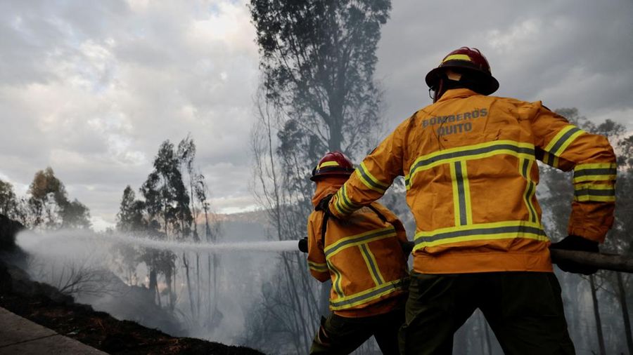 Kebakaran hutan di dekat kawasan permukiman, sementara orang-orang bermain sepak bola di sebuah lapangan di Quito, Ekuador, Minggu (13/9/2026). (REUTERS/Karen Toro)
