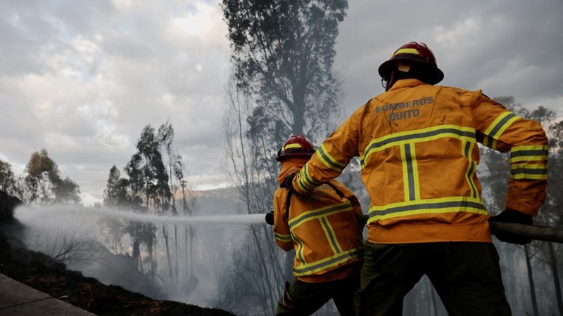 Kebakaran hutan di dekat kawasan permukiman, sementara orang-orang bermain sepak bola di sebuah lapangan di Quito, Ekuador, Minggu (13/9/2026). (REUTERS/Karen Toro)