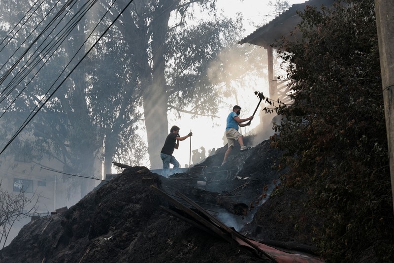 Kebakaran hutan di dekat kawasan permukiman, sementara orang-orang bermain sepak bola di sebuah lapangan di Quito, Ekuador, Minggu (13/9/2026). (REUTERS/Karen Toro)