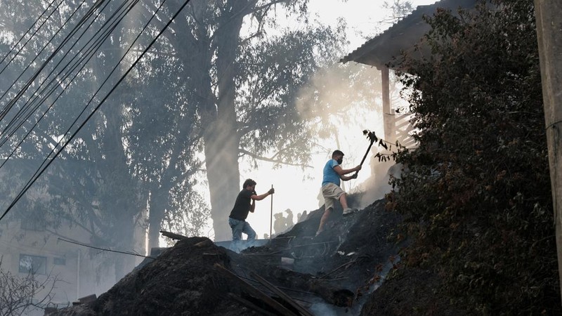 Kebakaran hutan di dekat kawasan permukiman, sementara orang-orang bermain sepak bola di sebuah lapangan di Quito, Ekuador, Minggu (13/9/2026). (REUTERS/Karen Toro)
