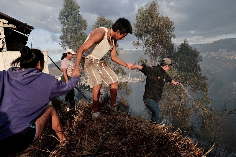 Kebakaran hutan di dekat kawasan permukiman, sementara orang-orang bermain sepak bola di sebuah lapangan di Quito, Ekuador, Minggu (13/9/2026). (REUTERS/Karen Toro)