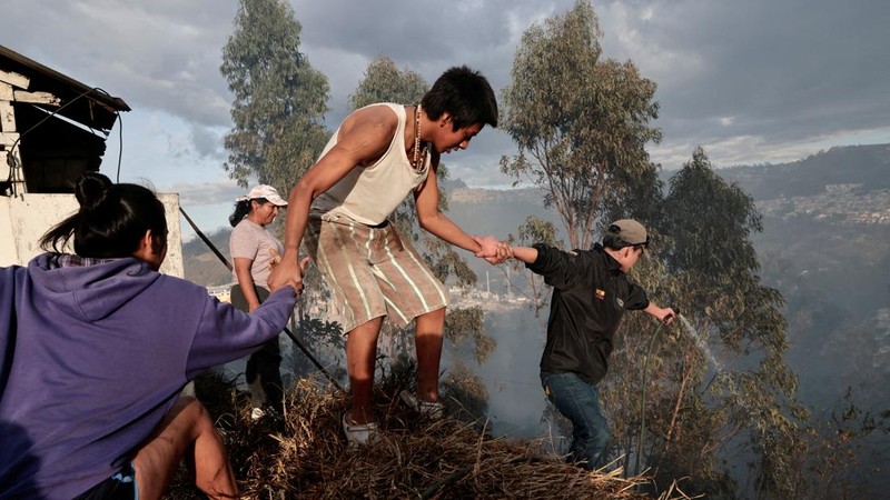 Kebakaran hutan di dekat kawasan permukiman, sementara orang-orang bermain sepak bola di sebuah lapangan di Quito, Ekuador, Minggu (13/9/2026). (REUTERS/Karen Toro)