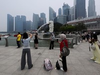 Wisatawan berfoto dengan latar belakang Merlion saat cakrawala kota diselimuti kabut asap akibat kebakaran hutan di wilayah sekitar yang mengurangi jarak pandang di seluruh negara kota kepulauan tersebut, di Singapura, 14 September 2026. (REUTERS/Suh