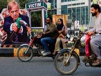 Pengendara sepeda motor melintas di dekat potret Perdana Menteri Pakistan Shehbaz Sharifyang dipasang sebagai bentuk protes terhadap kenaikan harga bahan bakar di tengah konflik AS-Iranmenjelang peluncuran nasional program pemerintah yang menawarkan