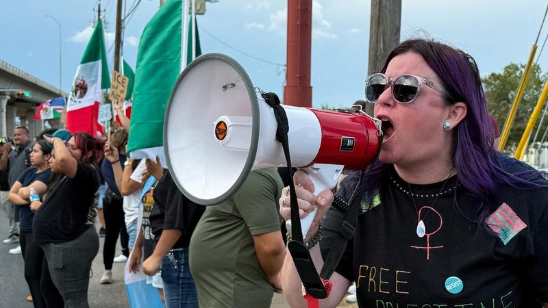 Seorang demonstran menggunakan pengeras suara sementara pengunjuk rasa lainnya mengibarkan bendera Meksiko—setelah seorang petugas imigrasi federal menembak dan melukai seorang pria—di Austin, Texas, AS, pada 20 September 2026, menurut keterangan pejabat kota. Foto diambil menggunakan ponsel.