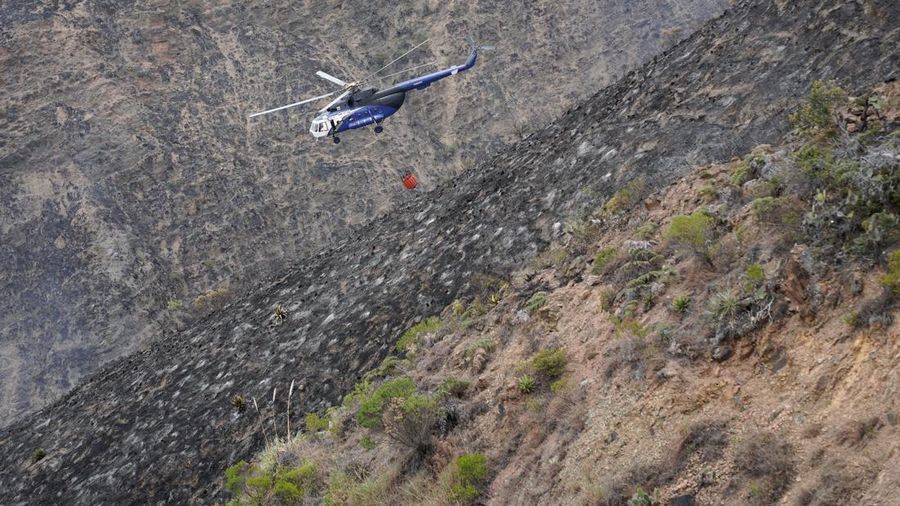 Sebuah helikopter yang membawa air terbang di atas lereng bukit yang hangus saat upaya pemadaman kebakaran hutan di Villa de Leyva, Kolombia, pada 21 September 2026.