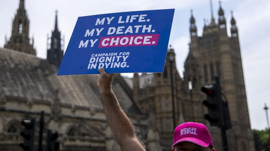A campaigner for a change in the law on assisted dying holds a placard outside The Palace of Westminster, home to the Houses of Parliament in central London, on June 20, 2025, as MPs hold a knife-edge vote on whether to allow assisted dying for termi