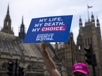 A campaigner for a change in the law on assisted dying holds a placard outside The Palace of Westminster, home to the Houses of Parliament in central London, on June 20, 2025, as MPs hold a knife-edge vote on whether to allow assisted dying for termi