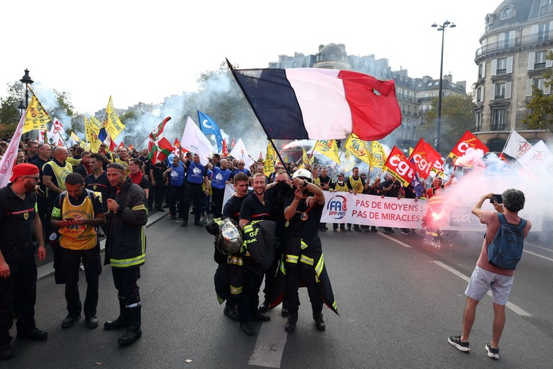 Petugas pemadam kebakaran Prancis membentangkan bendera Prancis saat unjuk rasa yang menuntut tambahan sumber daya dan pendanaan&mdash;menyusul musim panas yang diwarnai kebakaran hebat&mdash;di Paris sebagai bagian dari aksi mogok kerja dan protes oleh pekerja sektor publik di Prancis pada 29 September 2026. (REUTERS/Tom Nicholson)