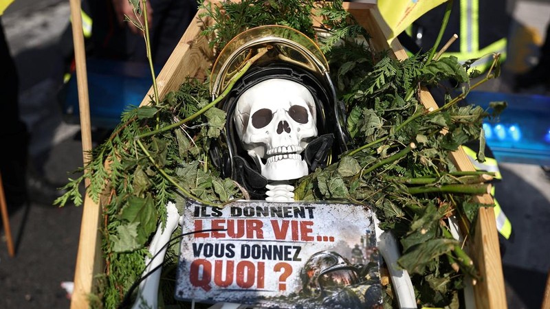 Sebuah replika peti mati berisi kerangka tiruan terlihat dalam aksi unjuk rasa petugas pemadam kebakaran Prancis yang menuntut tambahan sumber daya dan pendanaan—menyusul musim panas yang diwarnai kebakaran hebat—di Paris sebagai bagian dari hari pemogokan dan protes pekerja sektor publik di Prancis, 29 September 2026. Slogan tersebut berbunyi,