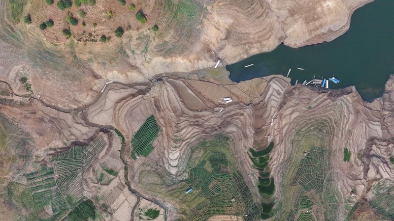 Warga melintas di dekat reruntuhan yang kembali muncul seiring surutnya permukaan air Waduk Jatigede akibat kekeringan di musim kemarau di Kabupaten Sumedang, Jawa Barat, Indonesia, Kamis (1/10/2026). (REUTERS/Claudio Pramana)