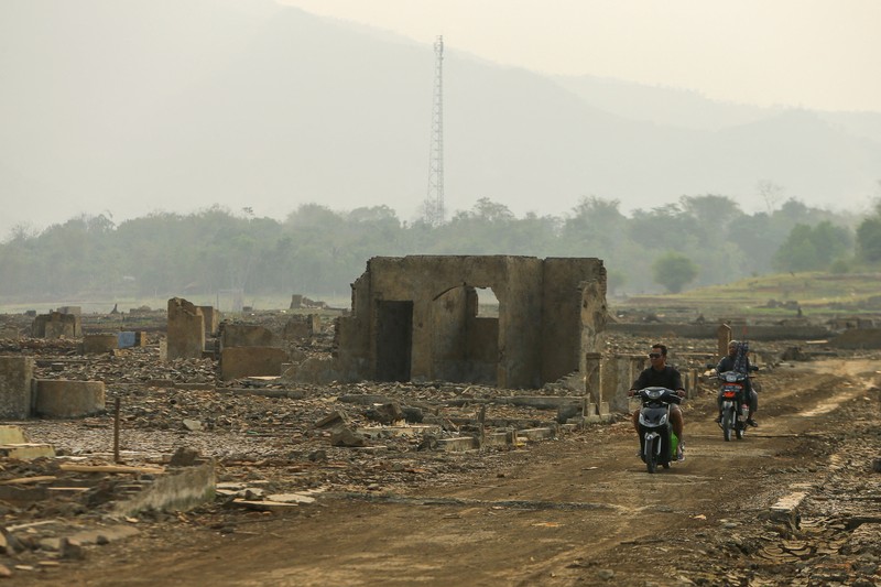 Warga melintas di dekat reruntuhan yang kembali muncul seiring surutnya permukaan air Waduk Jatigede akibat kekeringan di musim kemarau di Kabupaten Sumedang, Jawa Barat, Indonesia, Kamis (1/10/2026). (REUTERS/Claudio Pramana)