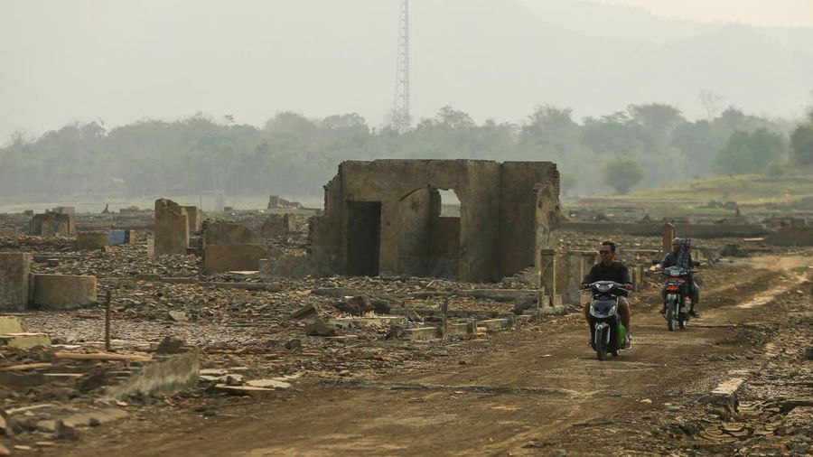 Warga melintas di dekat reruntuhan yang kembali muncul seiring surutnya permukaan air Waduk Jatigede akibat kekeringan di musim kemarau di Kabupaten Sumedang, Jawa Barat, Indonesia, Kamis (1/10/2026). (REUTERS/Claudio Pramana)