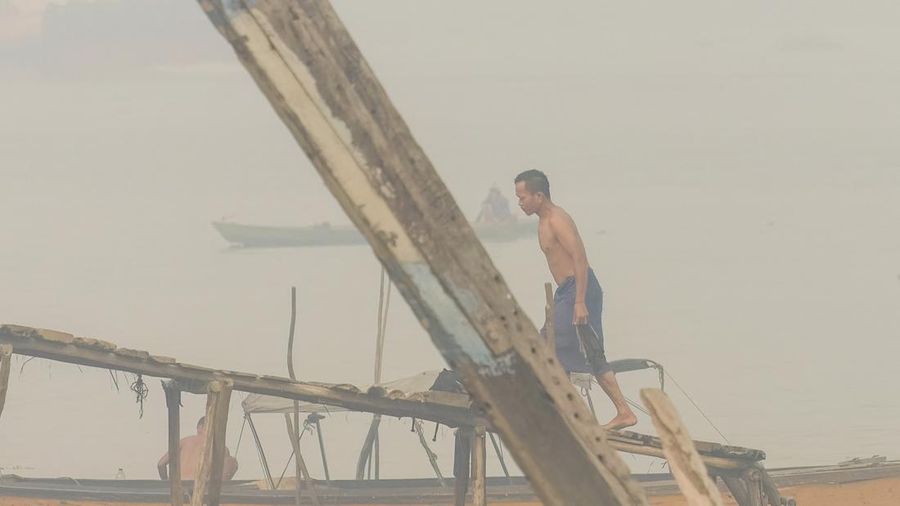 Seorang pria melintasi jembatan kayu setelah mandi di Sungai Musi saat kabut asap akibat kebakaran hutan dan lahan menyelimuti Palembang, Sumatra Selatan, pada 2 Oktober 2026. Kebakaran hutan dan lahan di Indonesia sebagian besar disebabkan oleh prak