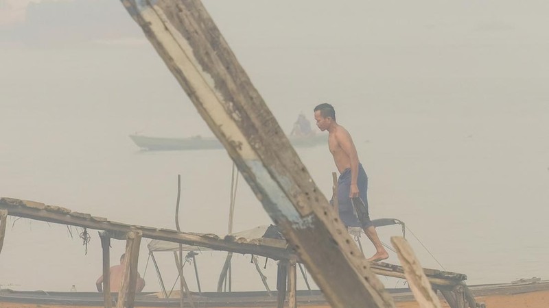 Seorang pria melintasi jembatan kayu setelah mandi di Sungai Musi saat kabut asap akibat kebakaran hutan dan lahan menyelimuti Palembang, Sumatra Selatan, pada 2 Oktober 2026. Kebakaran hutan dan lahan di Indonesia sebagian besar disebabkan oleh prak