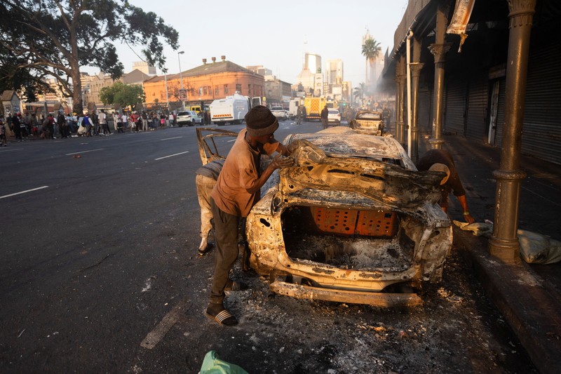 A police officer walks past burning vehicles during unrest following anti-migrant protests, where residents clashed with foreign-owned shopkeepers, and vehicles were set alight, after months of anti-migrant demonstrations that have drawn international criticism, in Soweto, South Africa, October 8, 2026. REUTERS/Stringer