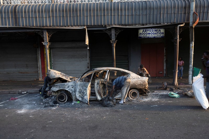 A police officer walks past burning vehicles during unrest following anti-migrant protests, where residents clashed with foreign-owned shopkeepers, and vehicles were set alight, after months of anti-migrant demonstrations that have drawn international criticism, in Soweto, South Africa, October 8, 2026. REUTERS/Stringer