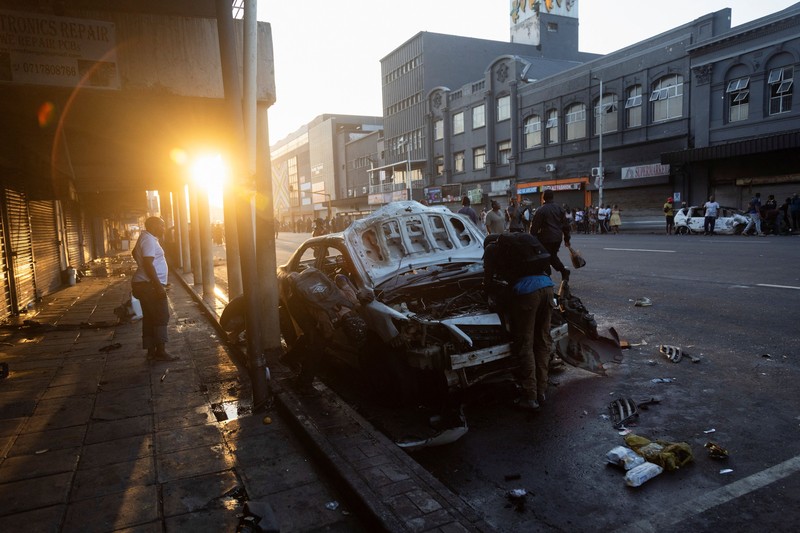 A police officer walks past burning vehicles during unrest following anti-migrant protests, where residents clashed with foreign-owned shopkeepers, and vehicles were set alight, after months of anti-migrant demonstrations that have drawn international criticism, in Soweto, South Africa, October 8, 2026. REUTERS/Stringer