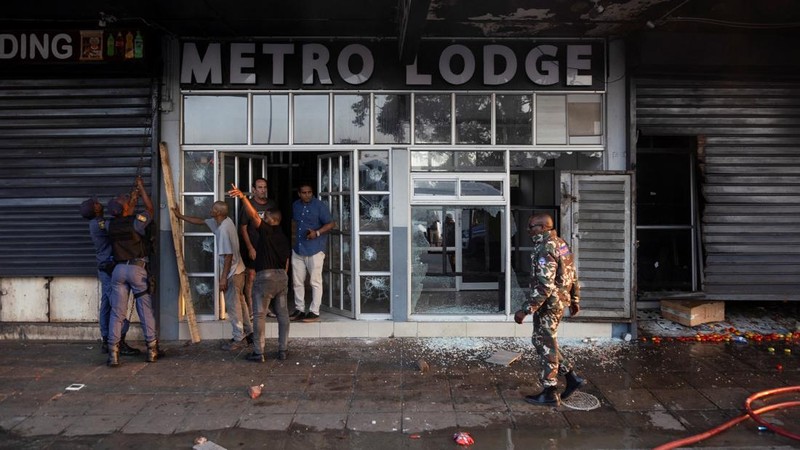 A police officer walks past burning vehicles during unrest following anti-migrant protests, where residents clashed with foreign-owned shopkeepers, and vehicles were set alight, after months of anti-migrant demonstrations that have drawn internationa