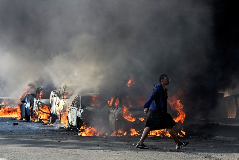 A police officer walks past burning vehicles during unrest following anti-migrant protests, where residents clashed with foreign-owned shopkeepers, and vehicles were set alight, after months of anti-migrant demonstrations that have drawn international criticism, in Soweto, South Africa, October 8, 2026. REUTERS/Stringer