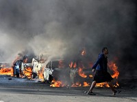 A police officer walks past burning vehicles during unrest following anti-migrant protests, where residents clashed with foreign-owned shopkeepers, and vehicles were set alight, after months of anti-migrant demonstrations that have drawn internationa