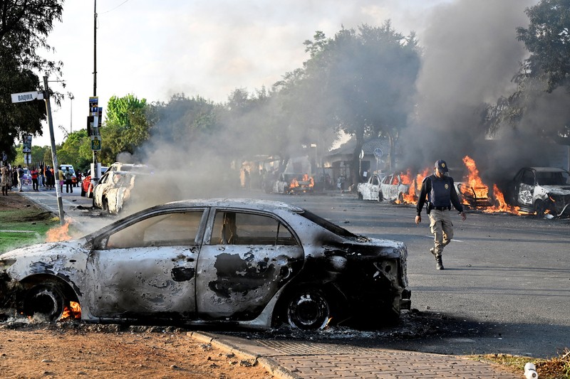 A police officer walks past burning vehicles during unrest following anti-migrant protests, where residents clashed with foreign-owned shopkeepers, and vehicles were set alight, after months of anti-migrant demonstrations that have drawn international criticism, in Soweto, South Africa, October 8, 2026. REUTERS/Stringer