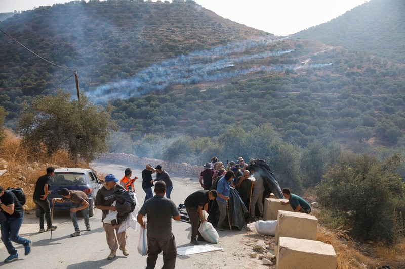Warga Palestina yang sedang memanen zaitun dan para aktivis asing bereaksi saat terjadi bentrokan dengan pemukim Israel di kebun zaitun milik warga Palestina di desa Deir Abu Mishal&mdash;dengan kepulan asap gas air mata terlihat di latar belakang&mdash;di dekat Ramallah, Tepi Barat yang diduduki Israel, pada 10 Oktober 2026. (REUTERS/Mohamad Torokman)