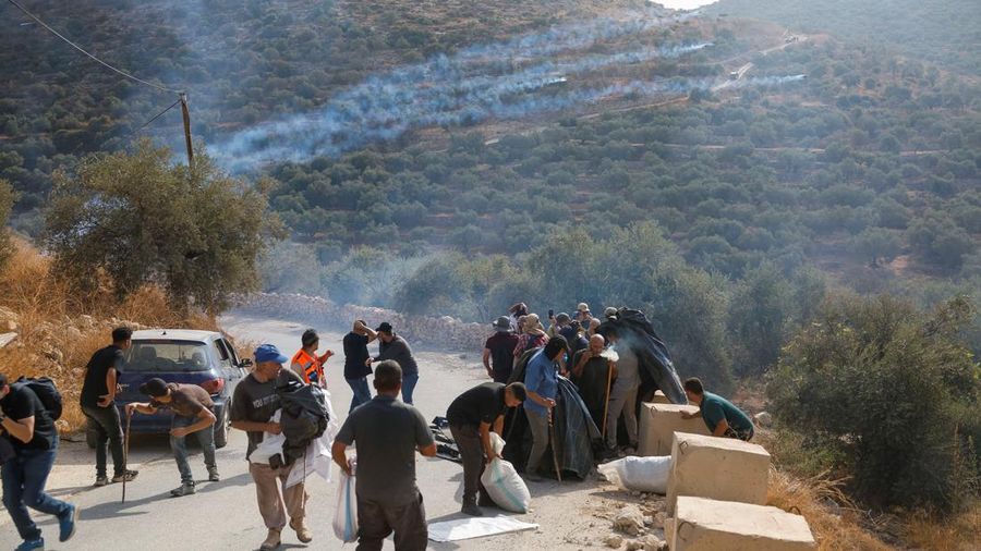 Warga Palestina yang sedang memetik zaitun pada musim panen bereaksi saat terjadi bentrokan dengan pemukim Israel di kebun zaitun milik warga Palestina di desa Deir Abu Mishal—dengan kepulan asap gas air mata terlihat di latar belakang—di dekat Ramallah, Tepi Barat yang diduduki Israel, pada 10 Oktober 2026.