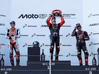 Pembalap Aprilia Racing Marco Bezzecchi merayakan kemenangan di atas podium sambil mengangkat trofi setelah memenangi balapan MotoGP Grand Prix Indonesia 2026, bersama pembalap Trackhouse MotoGP Team Raul Fernandez yang finis kedua dan pembalap April