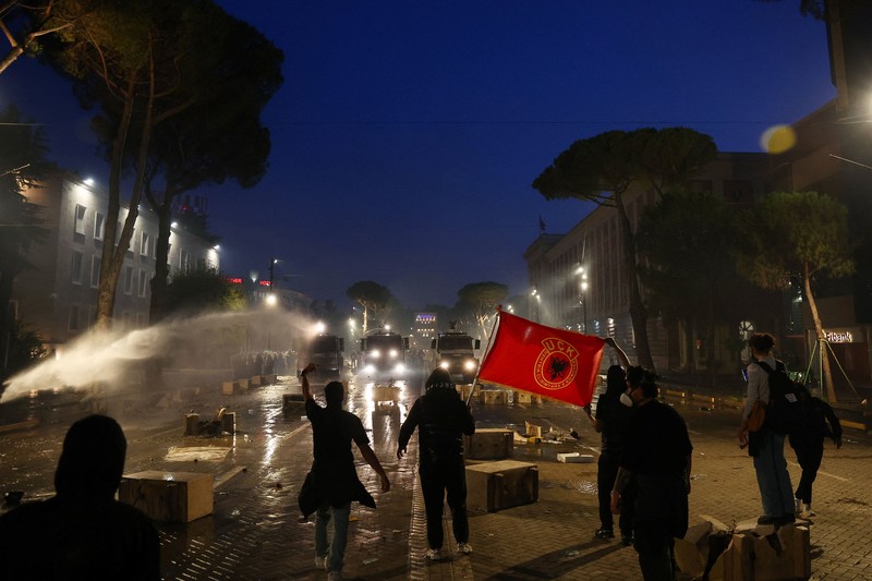 Orang-orang berkumpul di dekat api sementara gumpalan asap hitam membubung, di tengah aksi protes anti-pemerintah oleh para mahasiswa, di Tirana, Albania, 14 Oktober 2026. (REUTERS/Florion Goga)