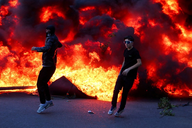 Orang-orang berkumpul di dekat api sementara gumpalan asap hitam membubung, di tengah aksi protes anti-pemerintah oleh para mahasiswa, di Tirana, Albania, 14 Oktober 2026. (REUTERS/Florion Goga)