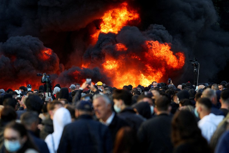 Orang-orang berkumpul di dekat api sementara gumpalan asap hitam membubung, di tengah aksi protes anti-pemerintah oleh para mahasiswa, di Tirana, Albania, 14 Oktober 2026. (REUTERS/Florion Goga)