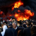 Orang-orang berkumpul di dekat api sementara gumpalan asap hitam membubung, di tengah aksi protes anti-pemerintah oleh para mahasiswa, di Tirana, Albania, 14 Oktober 2026. (REUTERS/Florion Goga)