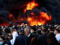 Orang-orang berkumpul di dekat api sementara gumpalan asap hitam membubung, di tengah aksi protes anti-pemerintah oleh para mahasiswa, di Tirana, Albania, 14 Oktober 2026. (REUTERS/Florion Goga)