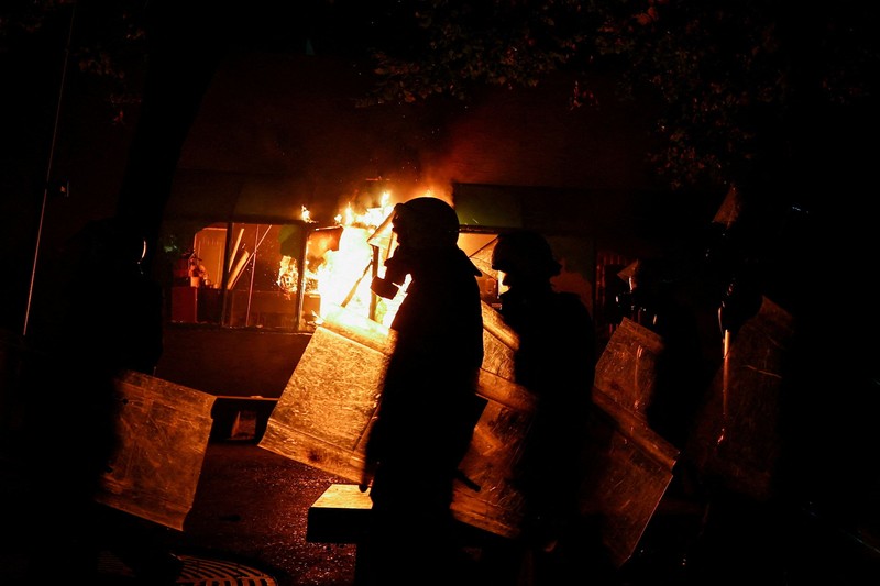 Orang-orang berkumpul di dekat api sementara gumpalan asap hitam membubung, di tengah aksi protes anti-pemerintah oleh para mahasiswa, di Tirana, Albania, 14 Oktober 2026. (REUTERS/Florion Goga)