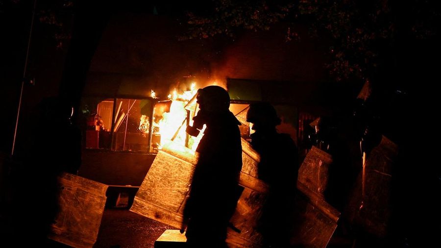 Polisi berjalan di luar Kementerian Kehakiman sementara kobaran api membubung di belakang mereka, di tengah aksi protes anti-pemerintah oleh para mahasiswa, di Tirana, Albania, 14 Oktober 2026.