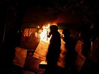 Polisi berjalan di luar Kementerian Kehakiman sementara kobaran api membubung di belakang mereka, di tengah aksi protes anti-pemerintah oleh para mahasiswa, di Tirana, Albania, 14 Oktober 2026. (REUTERS/Florion Goga)